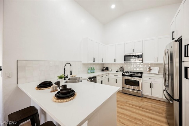 kitchen with a breakfast bar area, light wood-style flooring, appliances with stainless steel finishes, a sink, and a peninsula