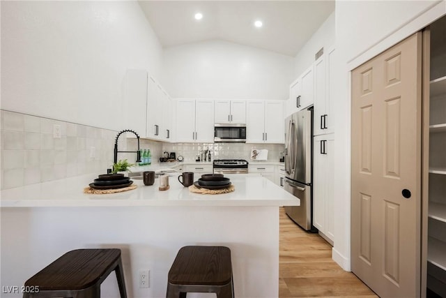 kitchen with a breakfast bar, a peninsula, vaulted ceiling, stainless steel appliances, and light countertops