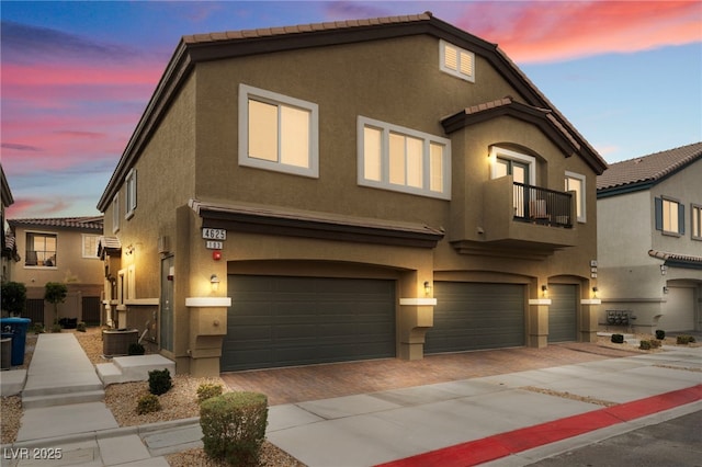 view of front of house with decorative driveway, stucco siding, an attached garage, a balcony, and cooling unit