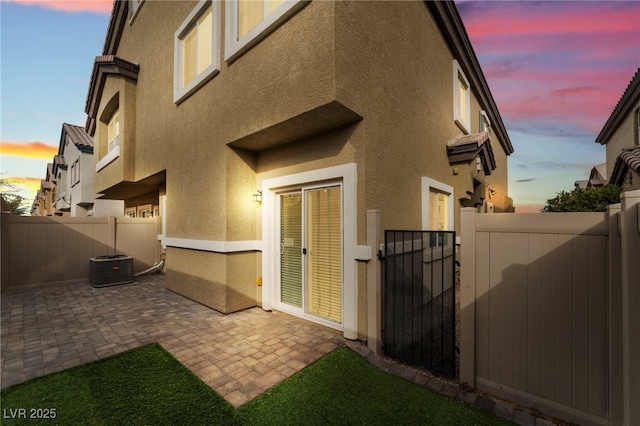 property exterior at dusk with stucco siding, a fenced backyard, a gate, and a patio