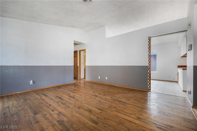 spare room featuring lofted ceiling, wood finished floors, visible vents, and baseboards