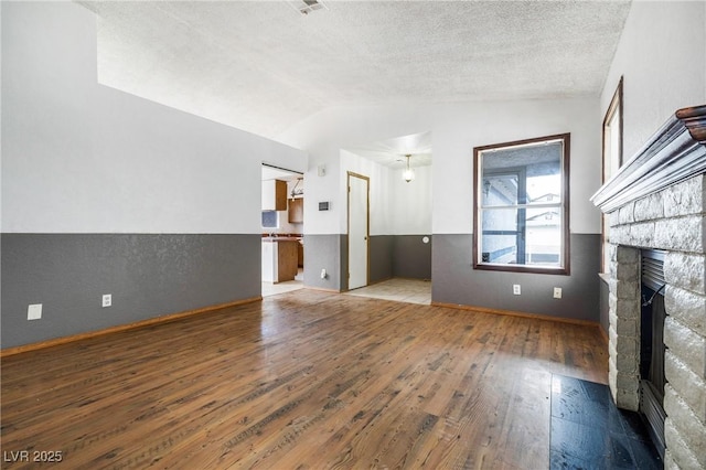 unfurnished living room with lofted ceiling, a fireplace, wood-type flooring, and a textured ceiling