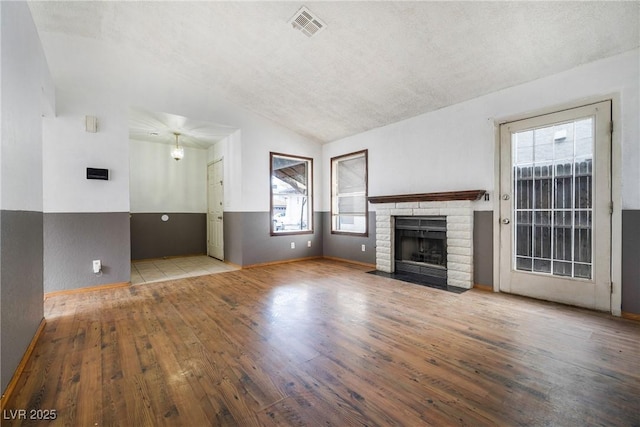 unfurnished living room with vaulted ceiling, a fireplace, visible vents, and wood-type flooring