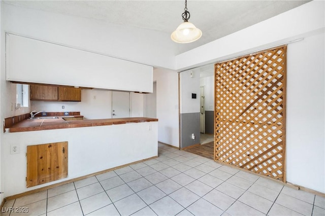 kitchen with a sink, light tile patterned flooring, tile countertops, and hanging light fixtures