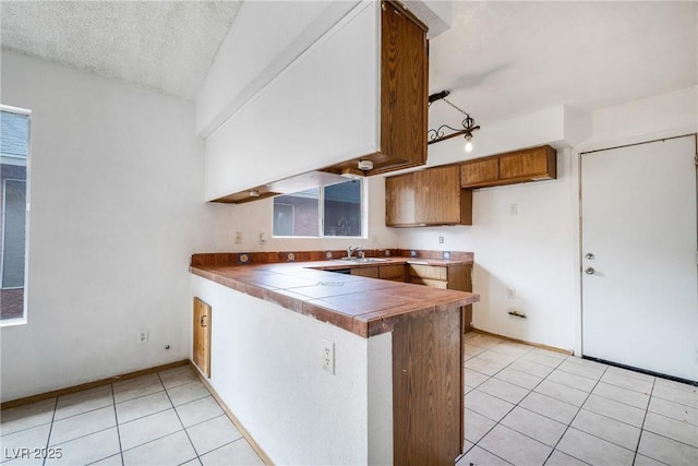 kitchen featuring light tile patterned floors, brown cabinets, a peninsula, a textured ceiling, and a sink