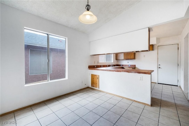 kitchen with light tile patterned floors, plenty of natural light, a peninsula, and lofted ceiling