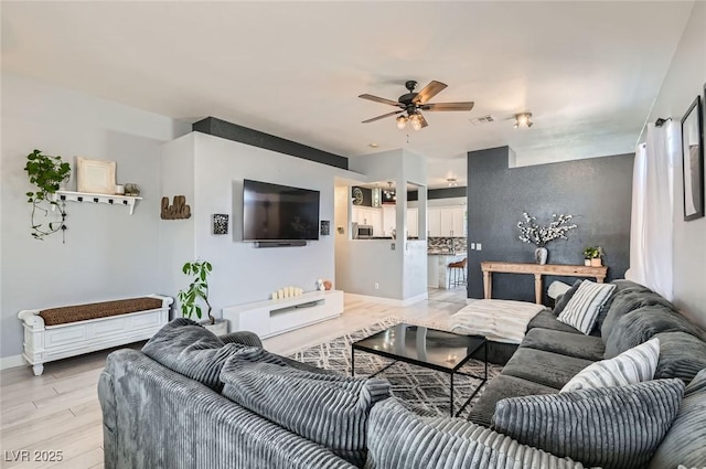 living area with visible vents, light wood-type flooring, a ceiling fan, and baseboards