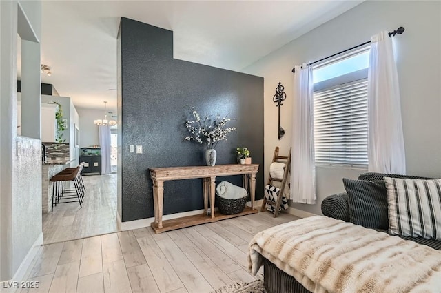 bedroom featuring light wood finished floors, an accent wall, baseboards, and a notable chandelier