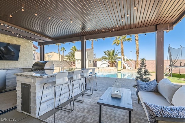 view of patio with a trampoline, a fenced in pool, an outdoor kitchen, a grill, and an outdoor living space