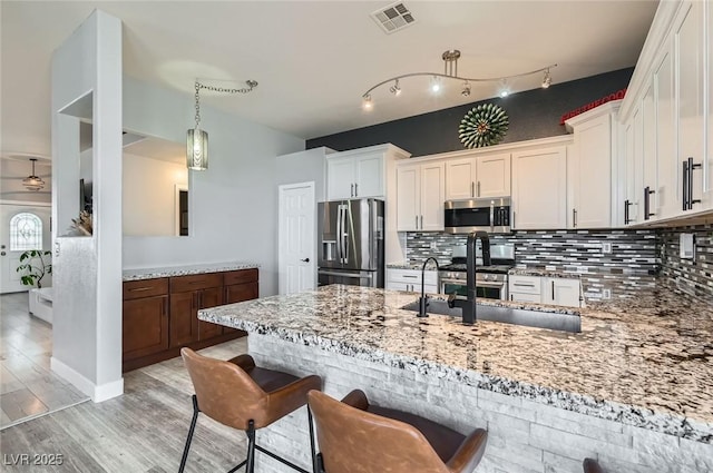 kitchen with appliances with stainless steel finishes, light wood-style floors, light stone counters, and tasteful backsplash