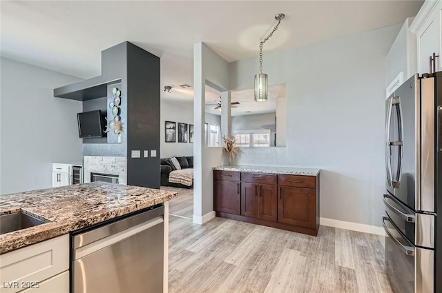 kitchen with light wood-style flooring, white cabinetry, appliances with stainless steel finishes, light stone countertops, and pendant lighting