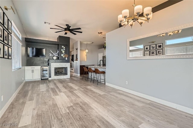 unfurnished living room featuring beverage cooler, ceiling fan with notable chandelier, wood finished floors, visible vents, and baseboards