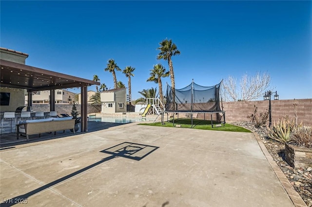 view of patio featuring a trampoline, a fenced backyard, and an outdoor pool