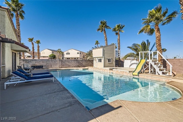 view of swimming pool featuring a patio area, a fenced backyard, a water slide, and an outdoor structure