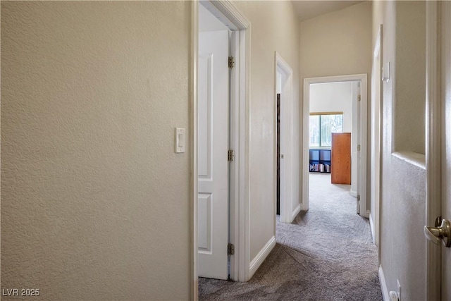 corridor with baseboards, carpet flooring, and a textured wall