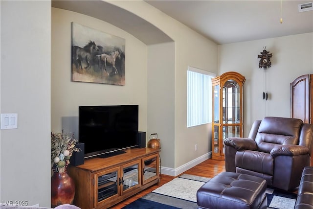 living area with arched walkways, wood finished floors, visible vents, and baseboards