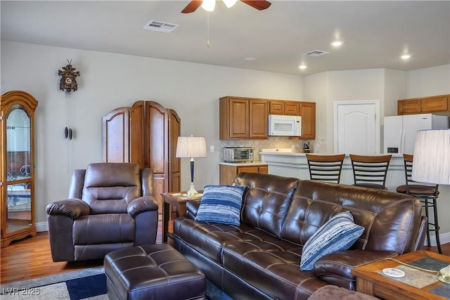 living area with a ceiling fan, a toaster, visible vents, and wood finished floors