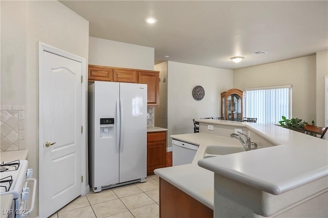 kitchen with light tile patterned floors, light countertops, brown cabinetry, a sink, and white appliances