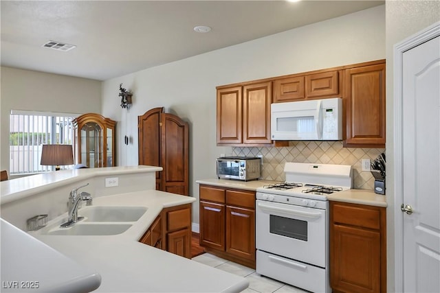 kitchen featuring visible vents, light countertops, backsplash, a sink, and white appliances