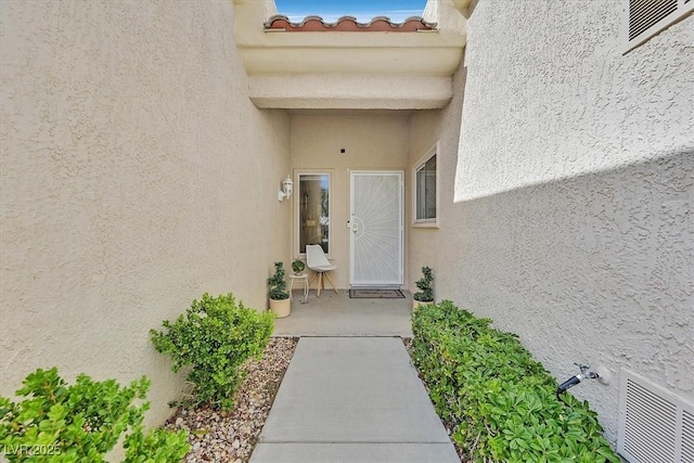 doorway to property with a tile roof, visible vents, and stucco siding