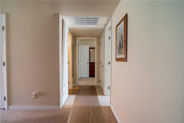 hall featuring light carpet, a textured wall, visible vents, and baseboards