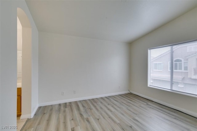 interior space featuring arched walkways, baseboards, vaulted ceiling, and light wood finished floors