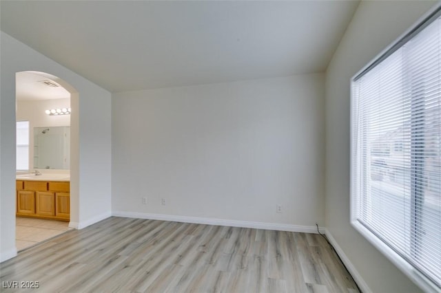 unfurnished room featuring baseboards, visible vents, arched walkways, light wood-style floors, and a sink