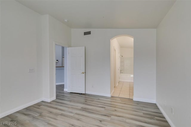 empty room with arched walkways, light wood-style flooring, visible vents, and baseboards