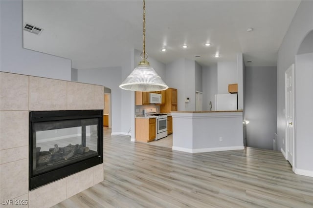 kitchen with light wood-style flooring, white appliances, a fireplace, visible vents, and hanging light fixtures