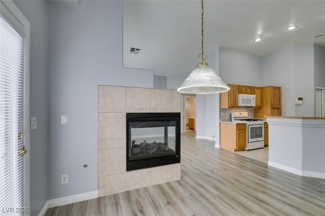 kitchen with a tile fireplace, white appliances, visible vents, baseboards, and light wood-type flooring