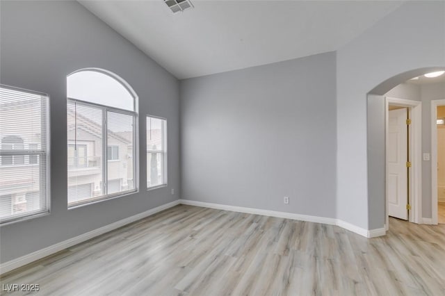 empty room featuring arched walkways, lofted ceiling, visible vents, baseboards, and light wood finished floors