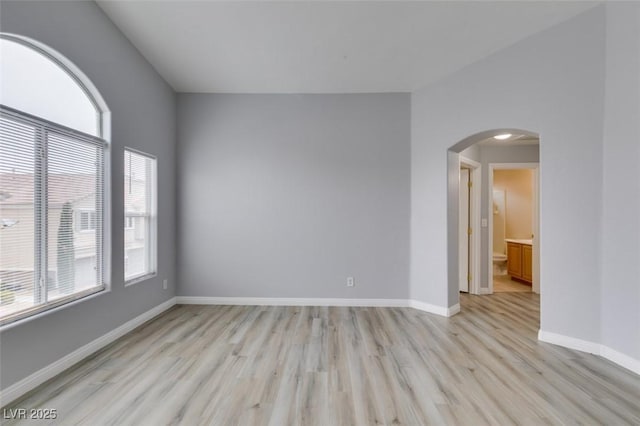 spare room with arched walkways, light wood-style flooring, and baseboards