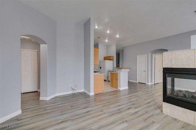 unfurnished living room featuring arched walkways, a fireplace, light wood-style flooring, and baseboards