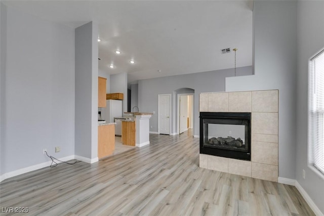 unfurnished living room with light wood finished floors, visible vents, baseboards, arched walkways, and a tile fireplace