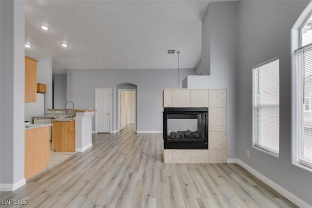 unfurnished living room with visible vents, baseboards, arched walkways, a tile fireplace, and light wood-style flooring