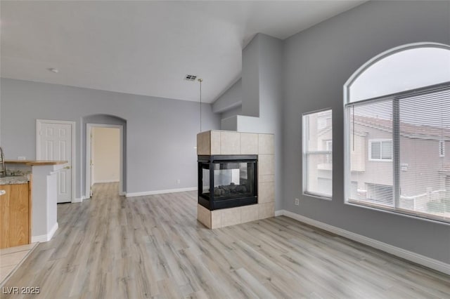 unfurnished living room with light wood-style floors, a tile fireplace, arched walkways, and baseboards