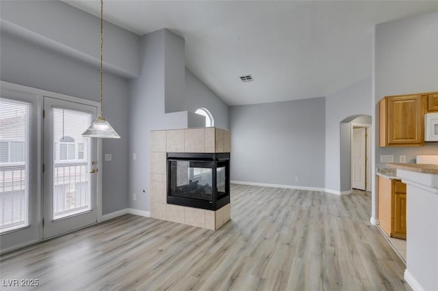 unfurnished living room featuring light wood-type flooring, a tiled fireplace, visible vents, and baseboards