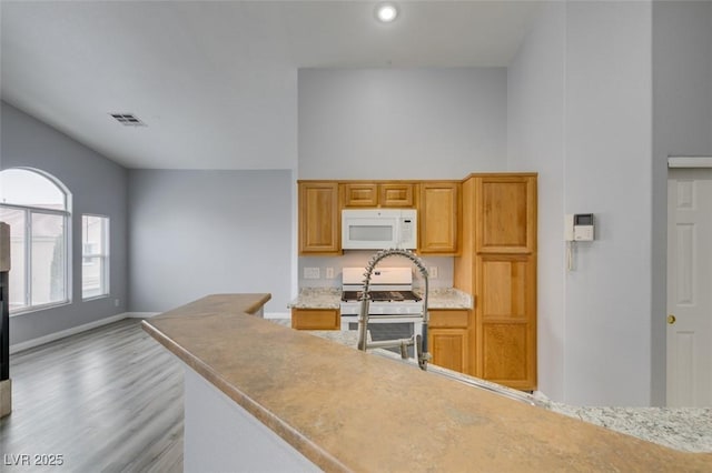 kitchen with high vaulted ceiling, white appliances, wood finished floors, visible vents, and baseboards