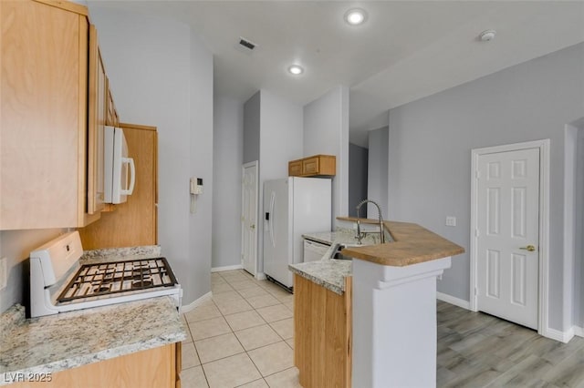 kitchen with light tile patterned floors, light countertops, a sink, white appliances, and a peninsula