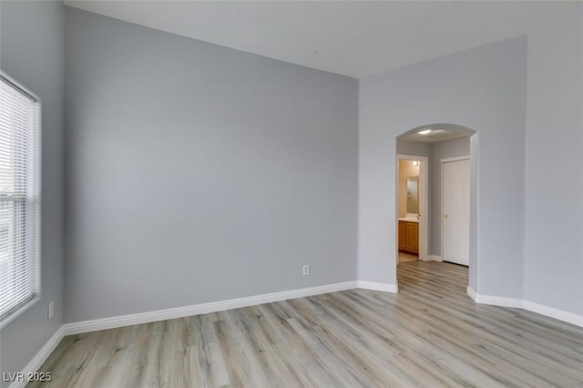 empty room with arched walkways, light wood-style flooring, and baseboards