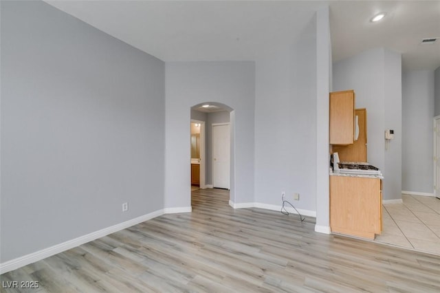 unfurnished living room featuring arched walkways, light wood finished floors, and baseboards