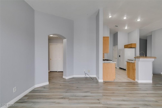 kitchen featuring arched walkways, white refrigerator with ice dispenser, light countertops, light wood-type flooring, and baseboards