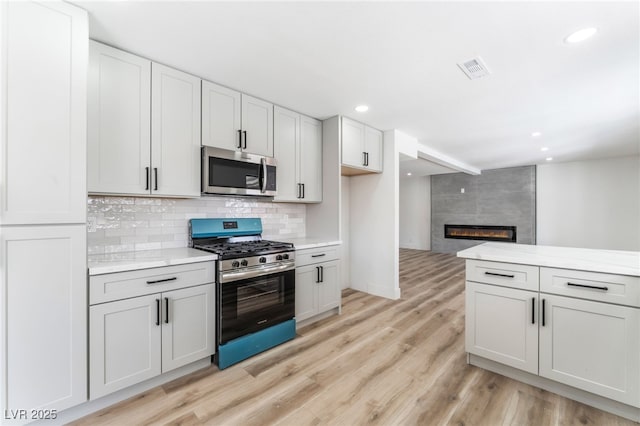 kitchen featuring visible vents, decorative backsplash, stainless steel appliances, light wood-type flooring, and a fireplace