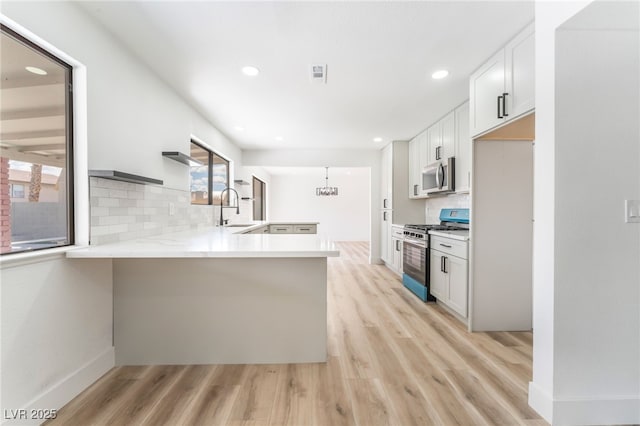 kitchen with light wood finished floors, backsplash, appliances with stainless steel finishes, white cabinets, and a peninsula