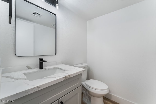 half bathroom with visible vents, toilet, vanity, wood finished floors, and baseboards