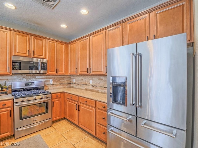 kitchen with light tile patterned floors, visible vents, appliances with stainless steel finishes, light stone countertops, and backsplash