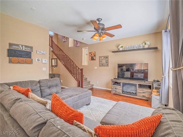 living room with a ceiling fan, wood finished floors, baseboards, and stairs