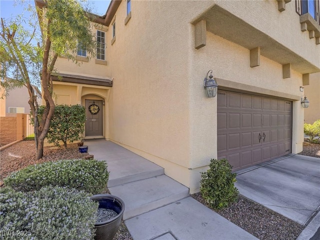 property entrance featuring driveway, an attached garage, fence, and stucco siding