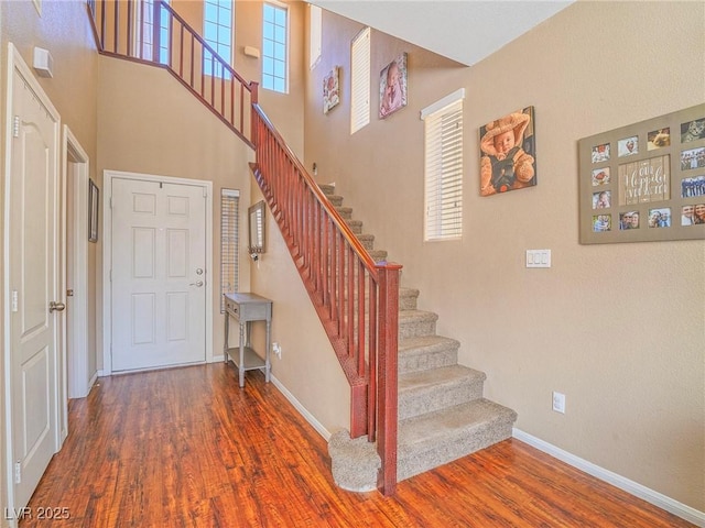 staircase featuring a high ceiling, baseboards, and wood finished floors