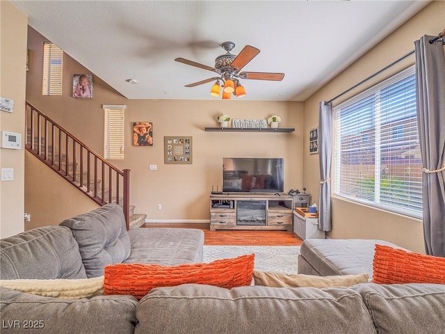 living area featuring stairs, ceiling fan, wood finished floors, and baseboards